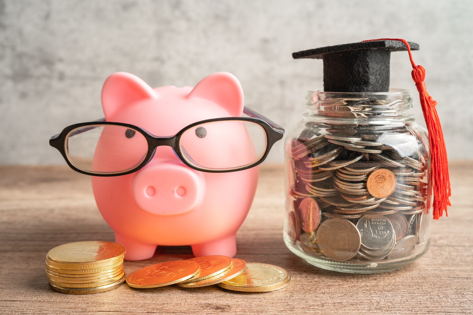 Pigging bank wearing eyeglass with coins and graduation hat; saving bank education concept.